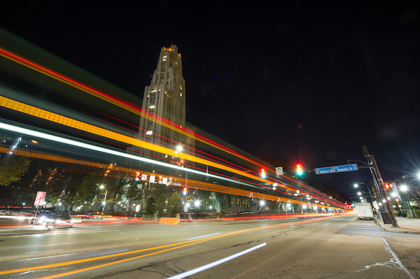 Low-angle shot of Pitt's Cathedral of Learning with blured traffic lights running along the street
